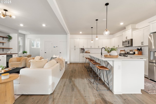 kitchen featuring open floor plan, an island with sink, light wood-style flooring, and stainless steel appliances