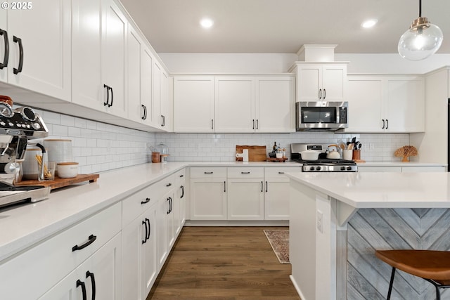 kitchen with wood finished floors, stove, light countertops, stainless steel microwave, and white cabinets