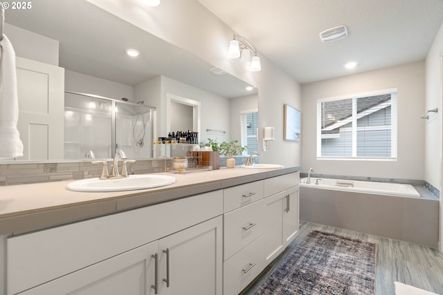bathroom featuring double vanity, a shower stall, a sink, and a garden tub