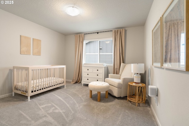 bedroom with a nursery area, light colored carpet, a textured ceiling, and baseboards