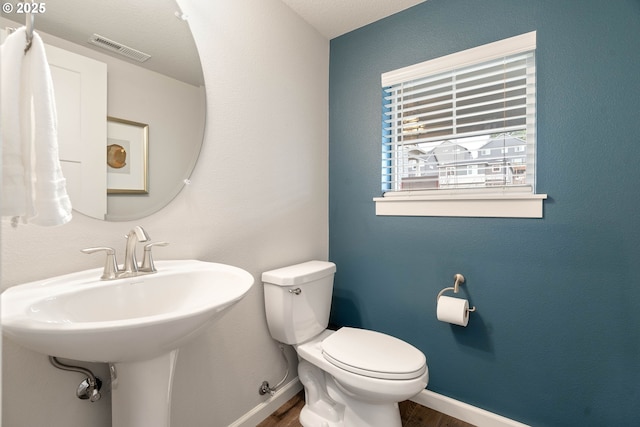 bathroom with baseboards, toilet, wood finished floors, and visible vents