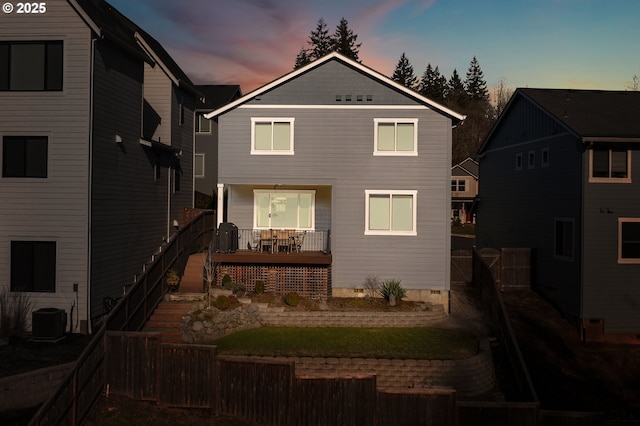 back of house at dusk with a fenced backyard and central AC