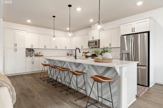 kitchen with a breakfast bar area, light countertops, hanging light fixtures, appliances with stainless steel finishes, and a sink