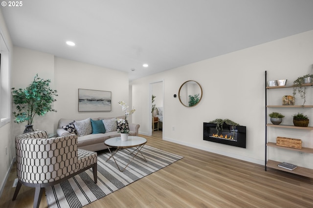 living room featuring a glass covered fireplace, recessed lighting, wood finished floors, and baseboards