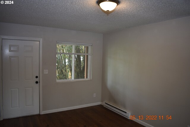 spare room with a baseboard heating unit, a textured ceiling, and dark hardwood / wood-style floors