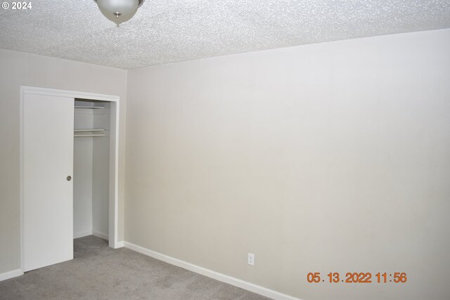 unfurnished bedroom featuring a textured ceiling, light colored carpet, and a closet