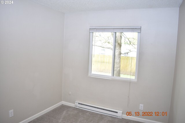 spare room with a baseboard radiator, a textured ceiling, a healthy amount of sunlight, and carpet