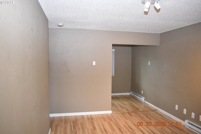 empty room featuring a textured ceiling, baseboard heating, and hardwood / wood-style flooring