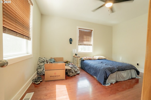bedroom with ceiling fan, multiple windows, wood finished floors, and visible vents