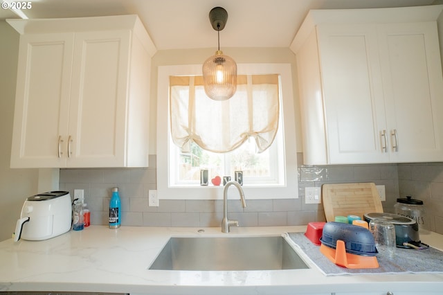 kitchen with light stone counters, a sink, white cabinetry, and tasteful backsplash