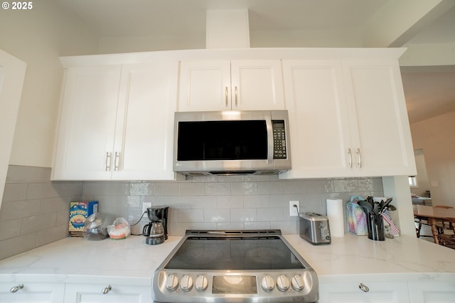 kitchen with backsplash, stainless steel appliances, light stone countertops, and white cabinetry