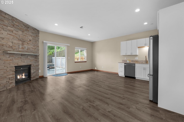unfurnished living room with recessed lighting, baseboards, dark wood finished floors, and a stone fireplace