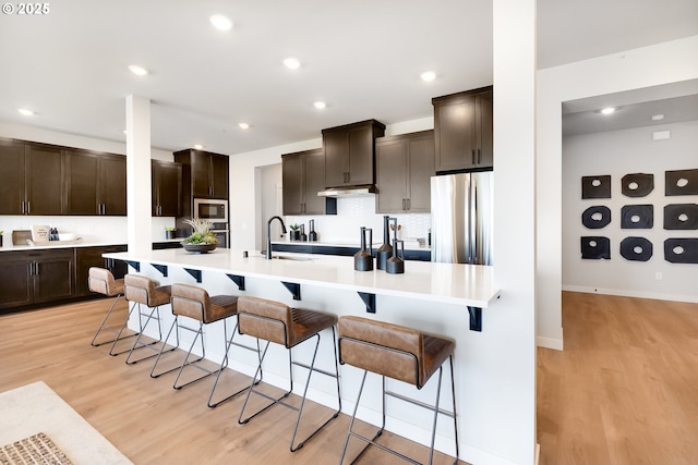 5591 N 87th Ave, Camas, WA 98607 - kitchen with stainless steel appliances, light wood-style flooring, a breakfast bar, dark brown cabinets, and recessed lighting