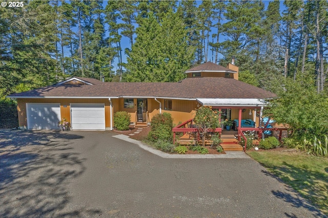 view of front of property with an attached garage, aphalt driveway, a chimney, and a porch