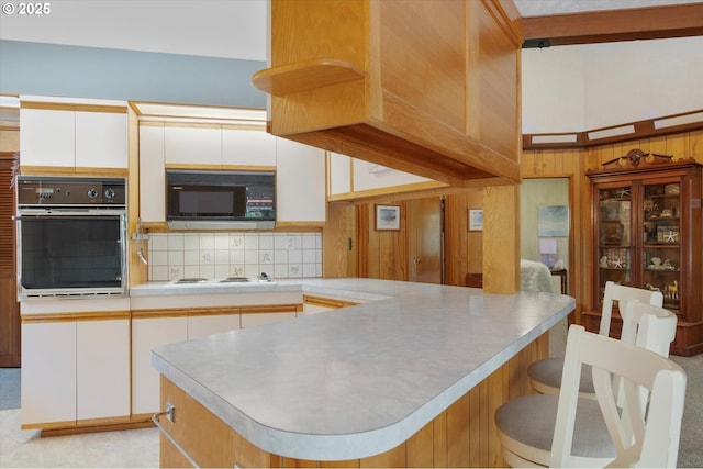 kitchen with light countertops, backsplash, wall oven, black microwave, and a peninsula