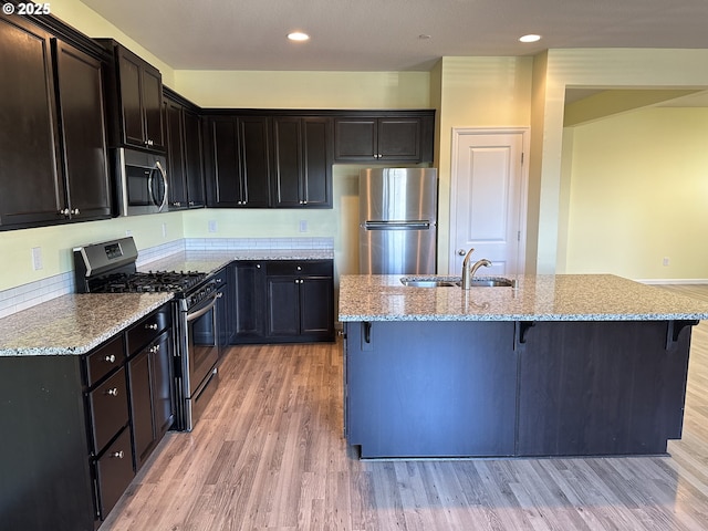 kitchen featuring stainless steel appliances, a sink, a breakfast bar, light stone counters, and light wood finished floors