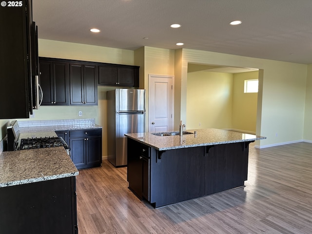 kitchen with freestanding refrigerator, a sink, range with gas stovetop, light stone countertops, and light wood-type flooring