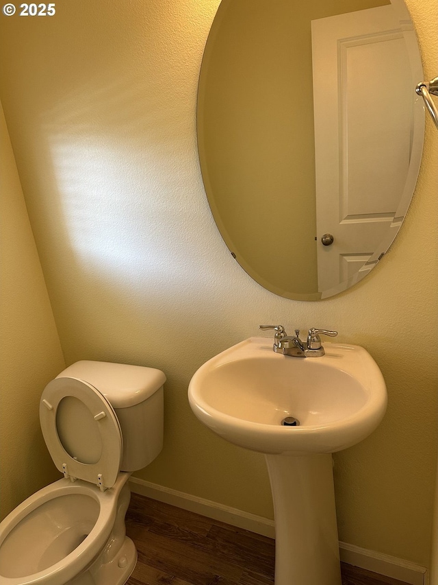 bathroom with toilet, wood finished floors, baseboards, and a sink