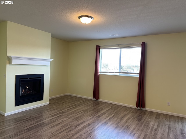 unfurnished living room featuring wood finished floors, baseboards, a fireplace, and a textured ceiling