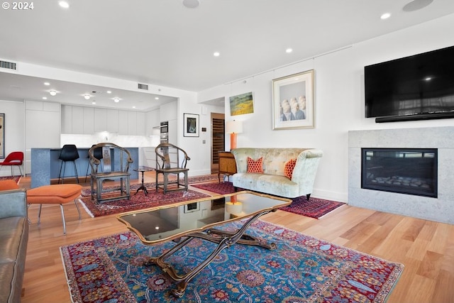 living area with a glass covered fireplace, recessed lighting, light wood-type flooring, and visible vents