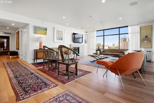 living area with a glass covered fireplace, floor to ceiling windows, recessed lighting, and wood finished floors