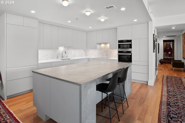 kitchen with visible vents, a kitchen island, modern cabinets, a kitchen breakfast bar, and a sink