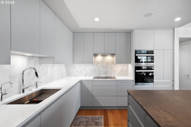 kitchen with backsplash, stovetop, modern cabinets, wood finished floors, and a sink