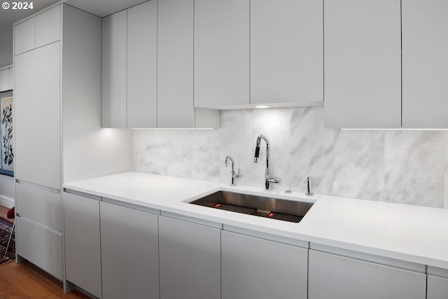 kitchen featuring wood finished floors, modern cabinets, light countertops, tasteful backsplash, and a sink