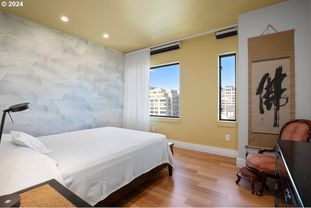 bedroom with recessed lighting, a view of city, light wood-style flooring, and baseboards