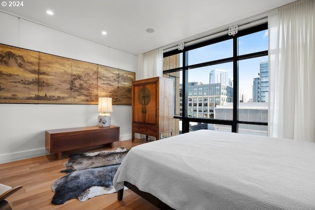 bedroom featuring baseboards, a city view, floor to ceiling windows, and wood finished floors