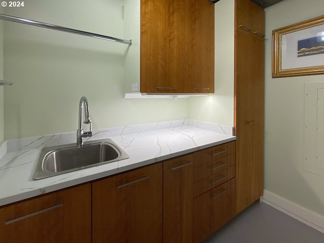 kitchen with a sink, baseboards, light stone countertops, and brown cabinets