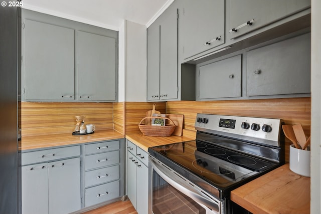 kitchen featuring stainless steel electric range oven, wood counters, decorative backsplash, and gray cabinetry