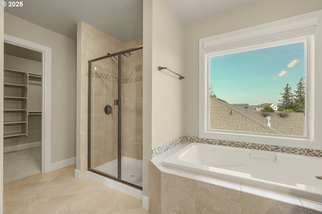 full bath with tile patterned flooring, a walk in closet, a garden tub, and a stall shower