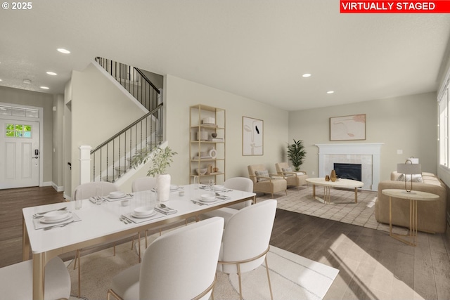 dining room with recessed lighting, dark wood-style flooring, stairway, and a tile fireplace