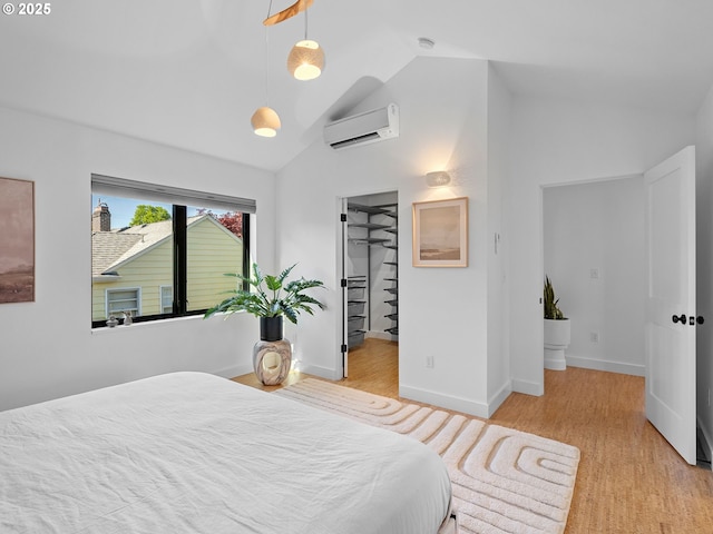bedroom with an AC wall unit, wood finished floors, high vaulted ceiling, a walk in closet, and baseboards