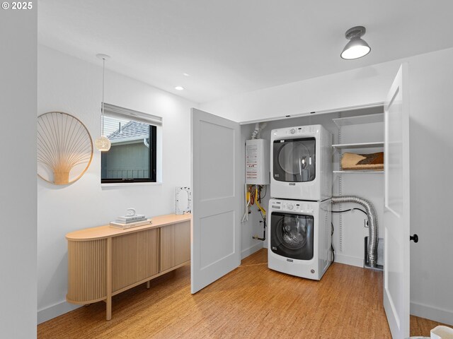 clothes washing area with estacked washer and dryer, light wood-type flooring, and baseboards
