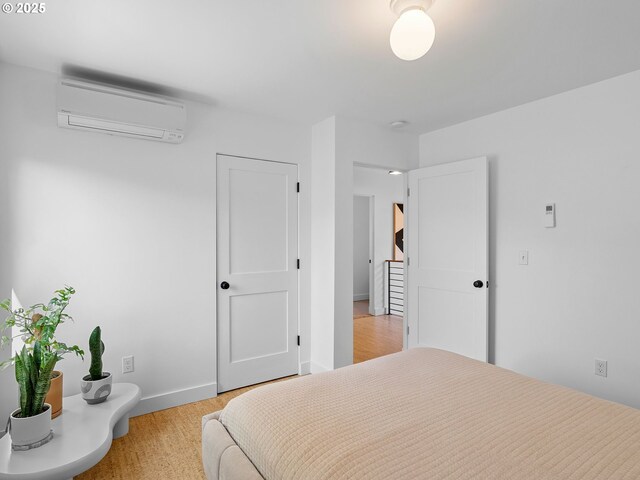 bedroom with a wall unit AC, light wood-type flooring, and baseboards