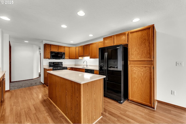 kitchen with black appliances, light wood-type flooring, light countertops, and a sink