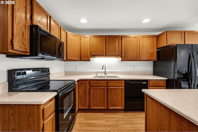 kitchen featuring a sink, light wood-type flooring, black appliances, and light countertops