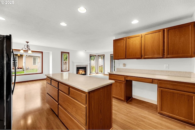 kitchen featuring light wood-type flooring, a kitchen island, brown cabinetry, and freestanding refrigerator