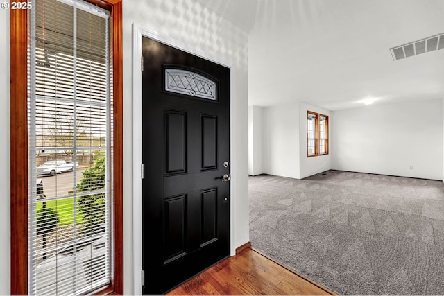 carpeted entrance foyer featuring visible vents and wood finished floors