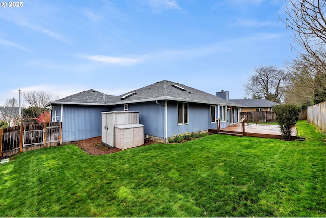 back of property with a deck, a fenced backyard, a lawn, and a shingled roof