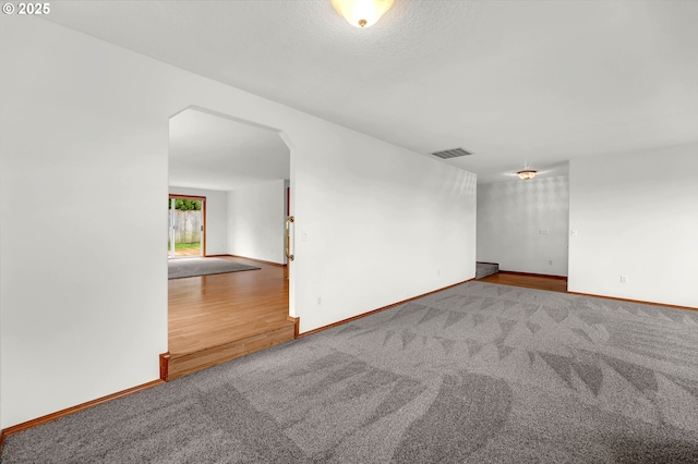 carpeted empty room with arched walkways, visible vents, and baseboards