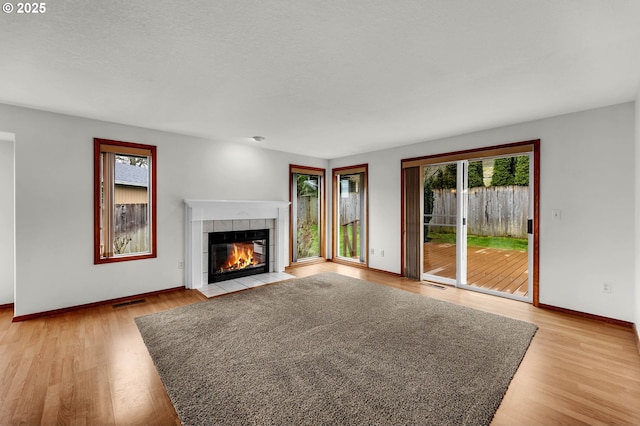 unfurnished living room featuring a tiled fireplace, a healthy amount of sunlight, light wood-style floors, and baseboards