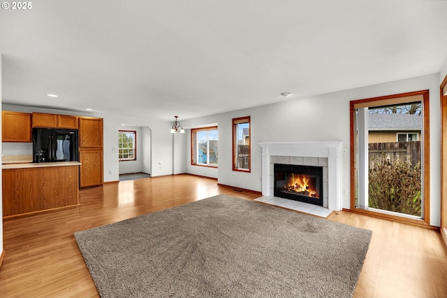 unfurnished living room featuring baseboards, light wood finished floors, recessed lighting, a tiled fireplace, and a chandelier