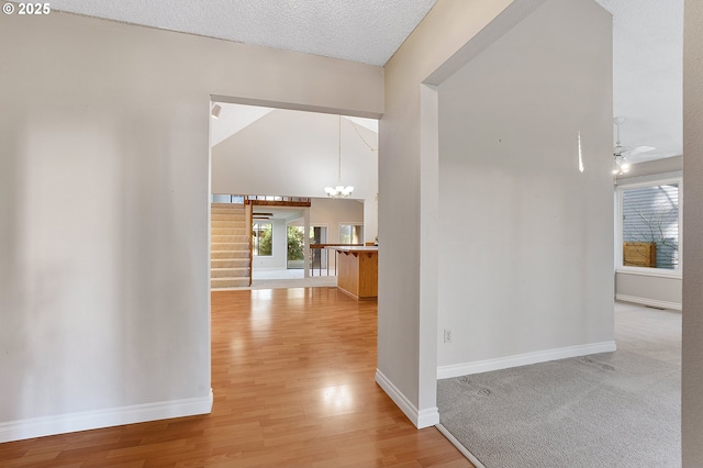 corridor with a notable chandelier, a towering ceiling, a textured ceiling, wood finished floors, and baseboards