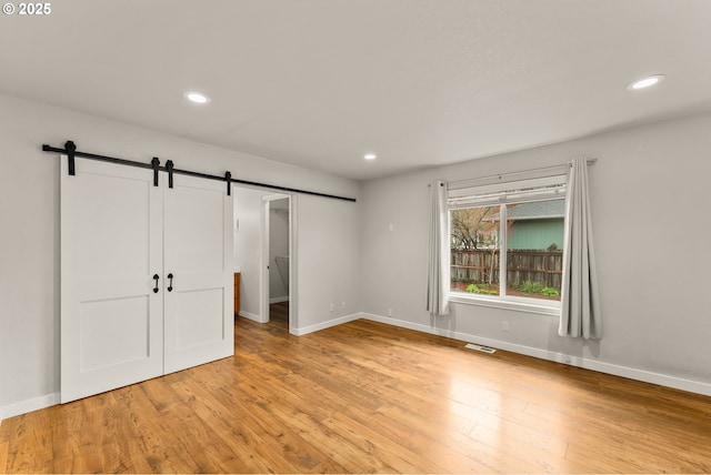 unfurnished bedroom with light wood finished floors, visible vents, baseboards, a barn door, and recessed lighting