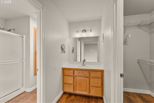 bathroom with a walk in closet, a stall shower, wood finished floors, baseboards, and vanity