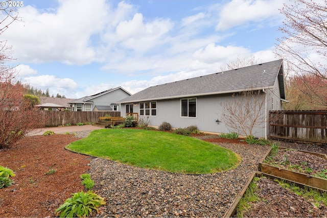 rear view of house featuring a shingled roof, a wooden deck, a lawn, a fenced backyard, and a garden