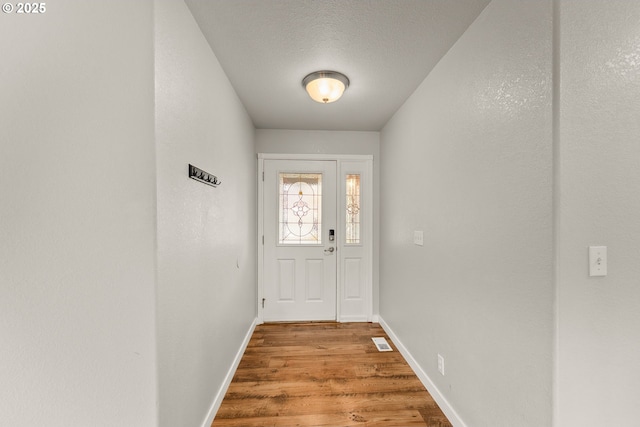 doorway to outside featuring a textured ceiling, wood finished floors, visible vents, and baseboards